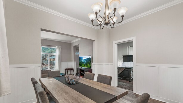 Une salle à manger avec une longue table en bois, six chaises, un lustre et une vue sur une montagne par la fenêtre.