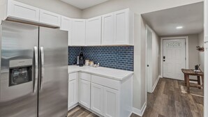 Une cuisine moderne avec des meubles blancs, un réfrigérateur en acier inoxydable et un pare-feu en carreaux bleus.