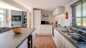 Une cuisine moderne avec un îlot central en bois, un four encastré et une fenêtre équipée de stores.