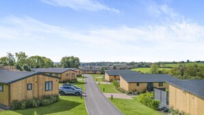 Une rangée de chalets en bois, avec une allée pavée, entourée de pelouses verdoyantes et d’arbres.
