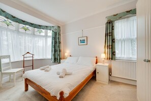 En pænt redt seng med sammenrullede håndklæder, en træstol, et natbord med en lampe og en radiator.
