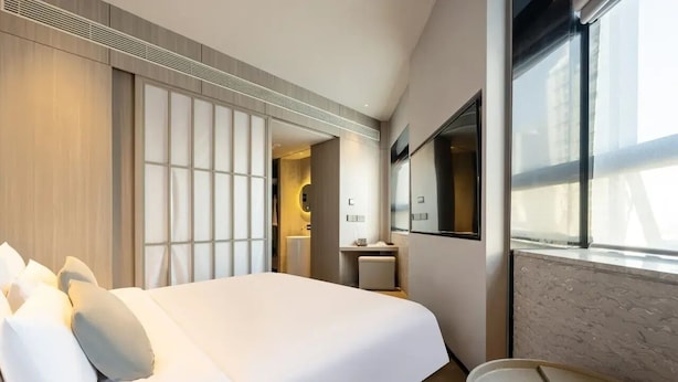 A modern hotel room with a large bed, a bedside table, a mirror, and a window with a view. - Beijing Bolly Wood Hotel-Guomao SKP  (Beijing)
