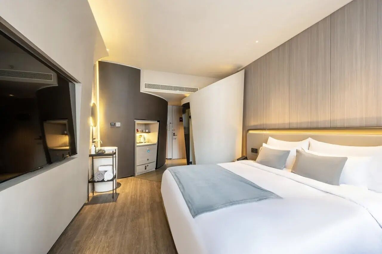 Une chambre d’hôtel moderne avec un grand lit, une table de chevet, un miroir et une armoire.