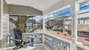 A covered porch with a view of the street, a chair, and a bottle of wine. - Downtown St. Michaels | Porch + Pet-Friendly (Saint Michaels)