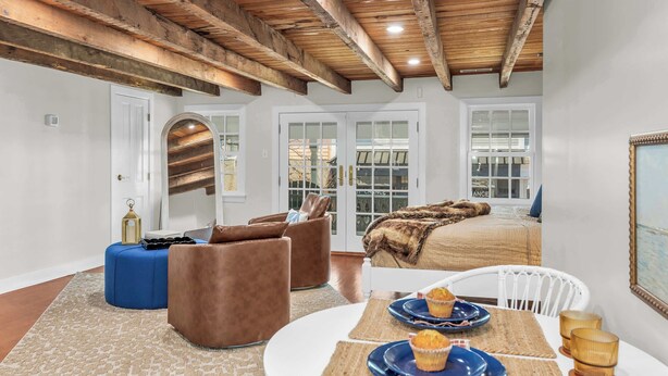 A modern living room with a high ceiling, wooden beams, a large window, and a cozy seating area with a fur throw. - Downtown St. Michaels | Porch + Pet-Friendly (Saint Michaels)