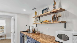 A kitchen with wooden shelves, a microwave, and a coffee maker. - Downtown St. Michaels | Porch + Pet-Friendly (Saint Michaels)