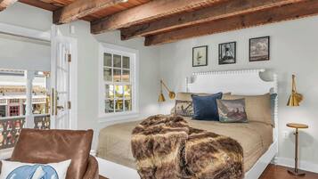 A bedroom with a large bed, a wooden ceiling, a window with a view of buildings, and a door.
