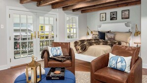 A bedroom with a bed, two leather chairs, a wooden ceiling, and a balcony with glass doors. - Downtown St. Michaels | Porch + Pet-Friendly (Saint Michaels)