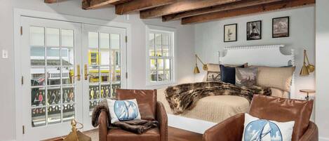 Un dormitorio con una cama, dos sillones de cuero, techo de madera y un balcón con puertas de vidrio.