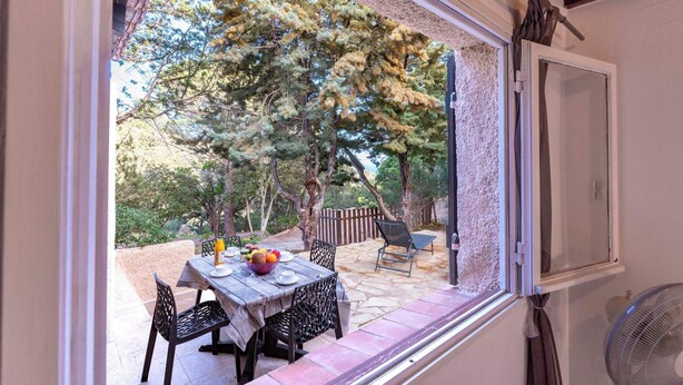 Une terrasse avec une table dressée pour le repas, entourée de chaises, et une vue sur des arbres et une clôture en bois.