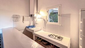Une cuisine de taille réduite, équipée d’une cuisinière à gaz, d’un évier et d’une fenêtre donnant sur un espace verdoyant.