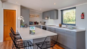 A modern kitchen with a central island, grey cabinets, and a window with blinds. - 2 Bed in Forest Of Dean (oc-t33299) (Coleford)