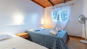 A bedroom with two beds, a wooden ceiling, a window with curtains, and a standing fan. - Villa "RoccaPina " 35m² - 2/4 pers, Rondinara, Bonifacio (Bonifacio)