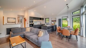 Uma sala de estar moderna com um sofá cinzento, uma mesa de centro de madeira e uma área de jantar com cadeiras laranja.