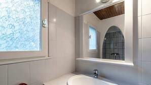 Ein Badezimmer mit einem weißen Waschbecken, einem Spiegel und einem Fenster.