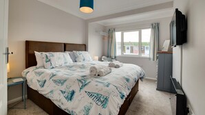 A bedroom with a large bed, a bedside table, a TV, and a window with curtains. - 4 Bed in Brixham (oc-bcharb) (Brixham)