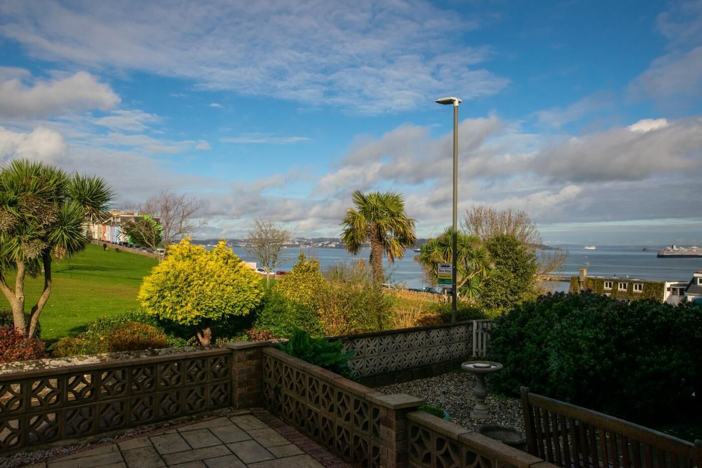 A patio with a decorative fence, a bird bath, and a view of the sea and buildings.