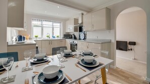 A modern kitchen with white cabinets, a dining area with a table set for four, and a built-in oven. - 4 Bed in Brixham (oc-bcharb) (Brixham)