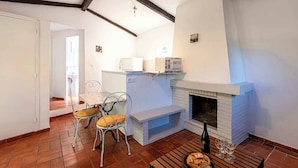 A cozy living room with a fireplace, a dining table with chairs, and a kitchen area with a refrigerator. - Villa "Lavezzi" 35m² - 2/4 pers, Rondinara, Bonifacio (Bonifacio)