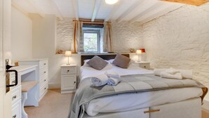 A bedroom with a stone wall, a bed with pillows, a nightstand with a lamp, and a dresser. - 1 Bed in Totnes (oc-bcbove) (Broadhempston)