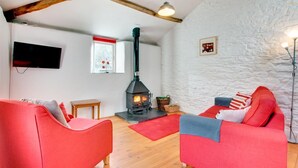 A cozy living room with a fireplace, red sofas, a wooden table, and a stone wall. - 1 Bed in Totnes (oc-bcbove) (Broadhempston)