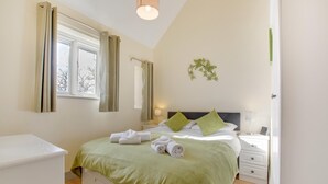 A neatly arranged bedroom with a bed, bedside tables, a lamp, and a window with curtains. - 2 Bed in Totnes (oc-bcteig) (Broadhempston)
