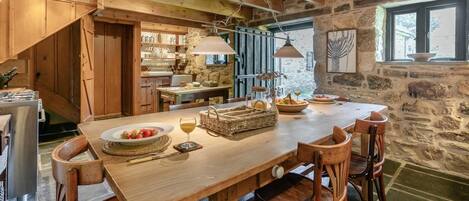 A rustic wooden dining area with a stone wall, a wooden staircase, and a kitchen visible in the background.