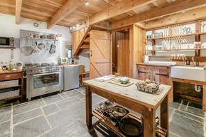 A rustic kitchen with wooden beams, a stone floor, a stove, a sink, and various kitchen utensils. - 1 Bed in St. Austell (oc-b33396) (Pentewan Valley)