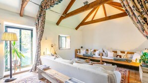 Um quarto aconchegante com sofá, um banco, uma mesa e uma janela com cortinas.