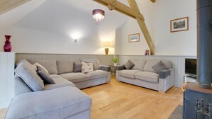 A cozy living room with two grey sofas, a wooden ceiling, a fireplace, and a small table with a lamp. - 3 Bed in Totnes (oc-bcplym) (Broadhempston)