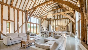Ein großzügiges Loft mit freiliegenden Holzbalken, einer modernen Sofagarnitur und einem Essbereich mit weißen Stühlen.