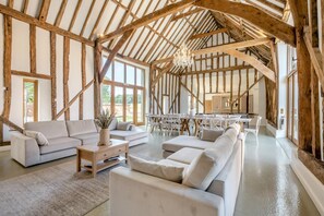 Ein großzügiges Loft mit freiliegenden Holzbalken, einer modernen Sofagarnitur und einem Essbereich mit weißen Stühlen.