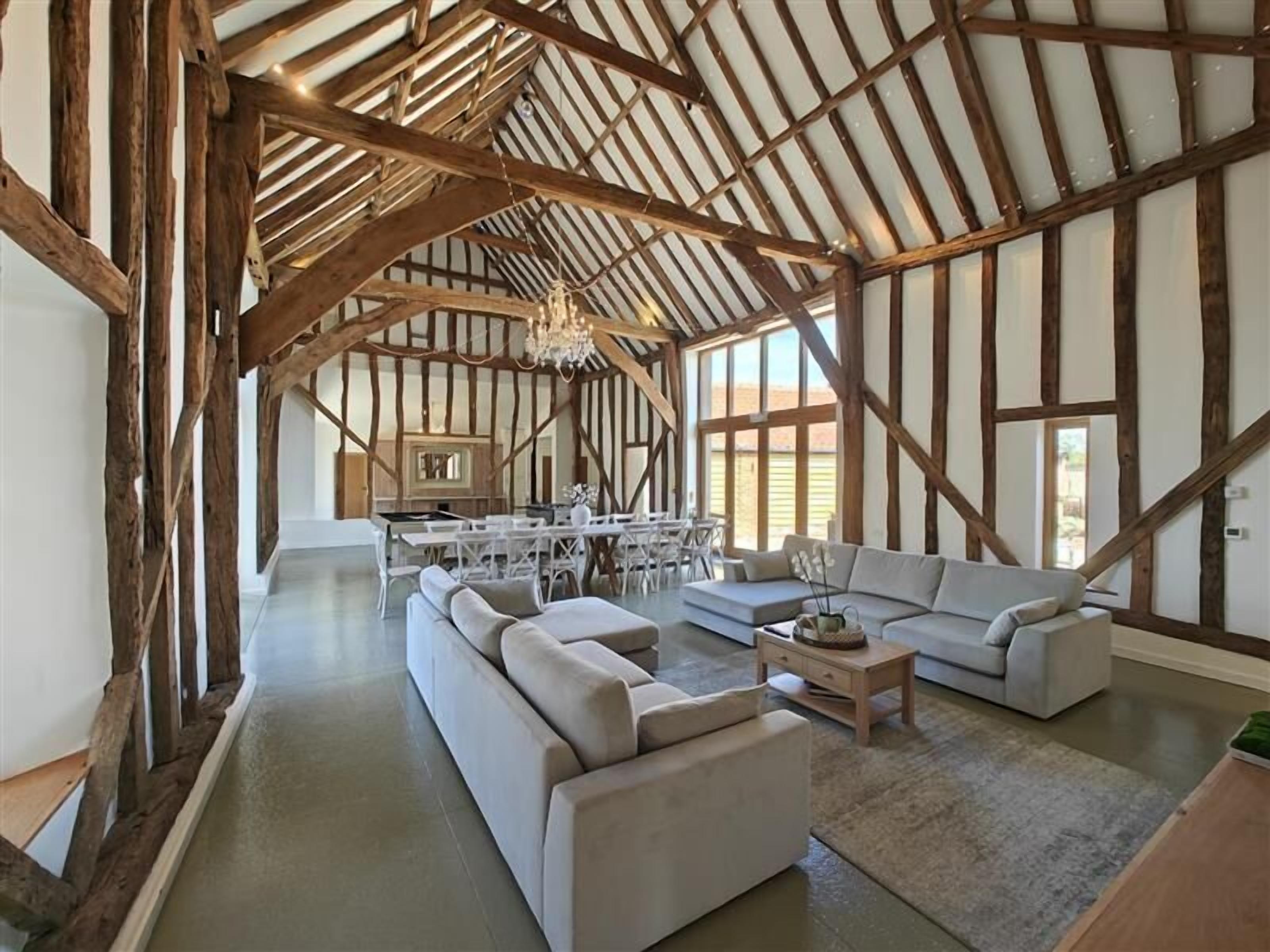 A spacious living area with exposed wooden beams, a large sofa set, and a dining table with chairs.