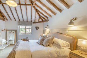 A bedroom with a large bed, wooden beams, a window, and a bedside table with a lamp. - 7 Bed in Ellough (oc-g33283) (Ellough)