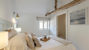 Ein Schlafzimmer mit einem Bett, Nachttischlampen, einem Fenster, einem Gemälde und einem rustikalen Deckenbalken.