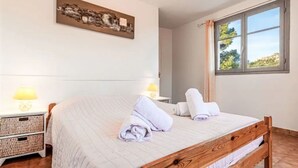 Una cama bien tendida con cabecera de madera, dos lámparas de noche, una obra de arte en la pared y una ventana con cortinas.
