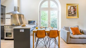 Una cocina moderna con una isla central, un comedor con sillas naranjas y un sofá gris con un cojín naranja.