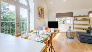 Un espacio habitable amplio con una mesa de comedor lista para el desayuno, un televisor de pantalla plana y una zona de estar acogedora con un sofá y sillones.