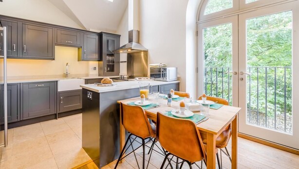 Una cocina moderna con armarios oscuros, una isla central y un comedor con vista a un balcón.