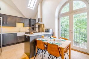 Une cuisine moderne avec des meubles de couleur sombre, un îlot central et un coin repas donnant sur un balcon.