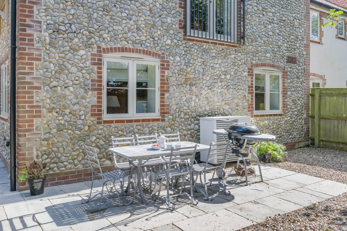 A patio area with a stone wall, a grill, a table with chairs, and a potted plant.