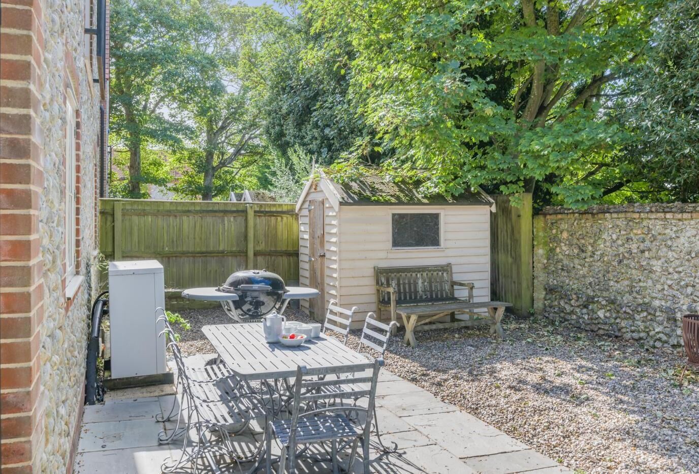 Une terrasse avec un barbecue, une table et des chaises, un abri de jardin et un mur en pierre.
