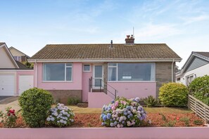 Ein eingeschossiges Haus mit Ziegeldach, Hauseingang und kleinem Vorgarten mit Blumenbeeten.
