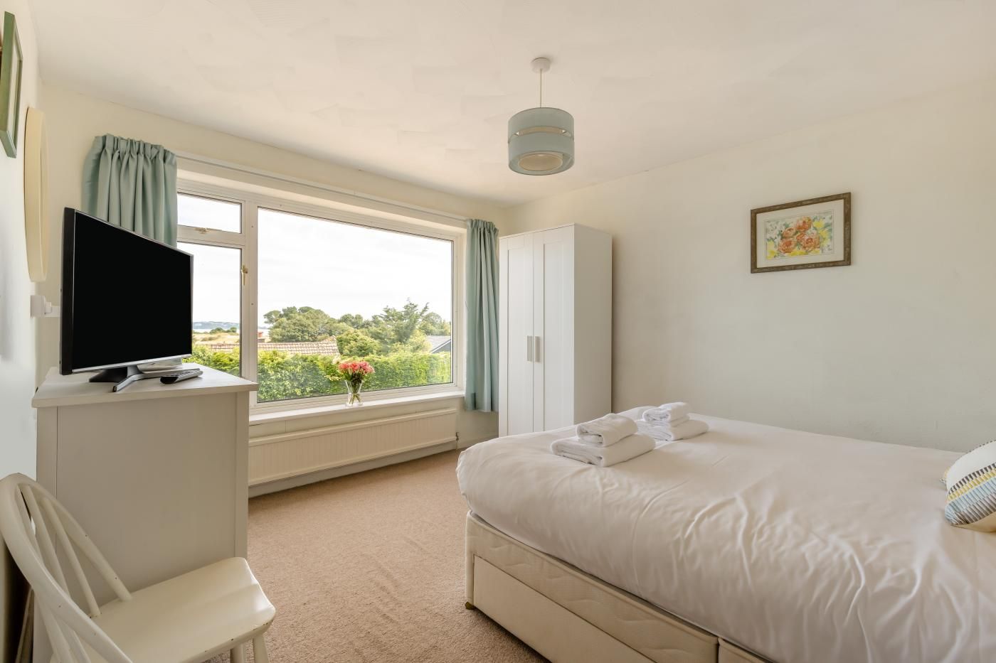 Hotelkamer met een bed, een televisie op een standaard, een stoel, een kast en een raam met uitzicht op groen.