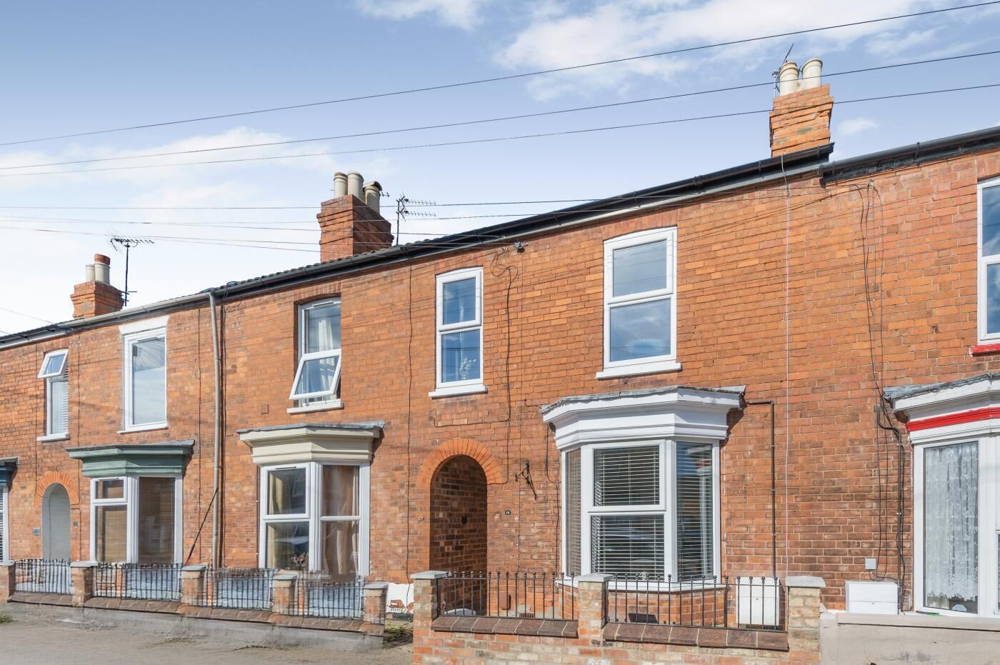 A row of red brick terraced houses with white-framed windows and a central archway.