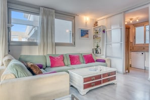 A living room with a sofa, a coffee table, a bookshelf, and a window with curtains. - Apartment 'Elegance Denia 4' with Shared Pool, Wi-Fi and Air Conditioning (Denia)