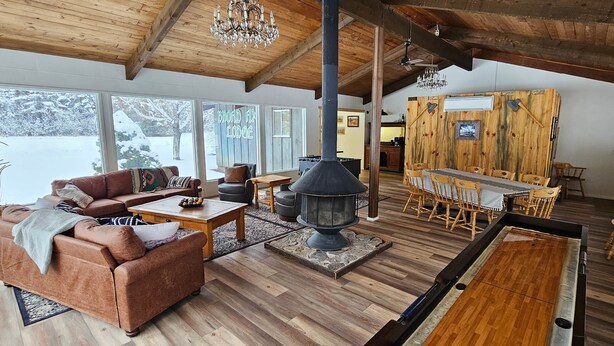 Ein gemütliches Lodge-Interieur mit Kamin, Holzmöbeln und großen Fenstern mit Blick auf die verschneite Landschaft.