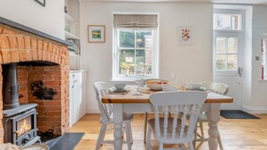 A dining area with a brick fireplace, white chairs, a wooden table, and a window with a view of the outdoors. - 2 Bed in West Lulworth (oc-j33448) (West Lulworth)