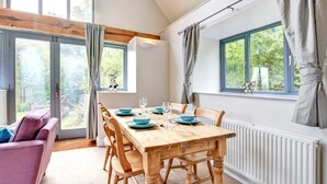 Un comedor con una mesa de madera preparada para cuatro personas, un sofá morado y ventanas grandes con cortinas.