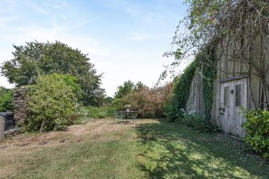 Un jardín con una silla de metal, un muro de piedra y un cobertizo de madera.